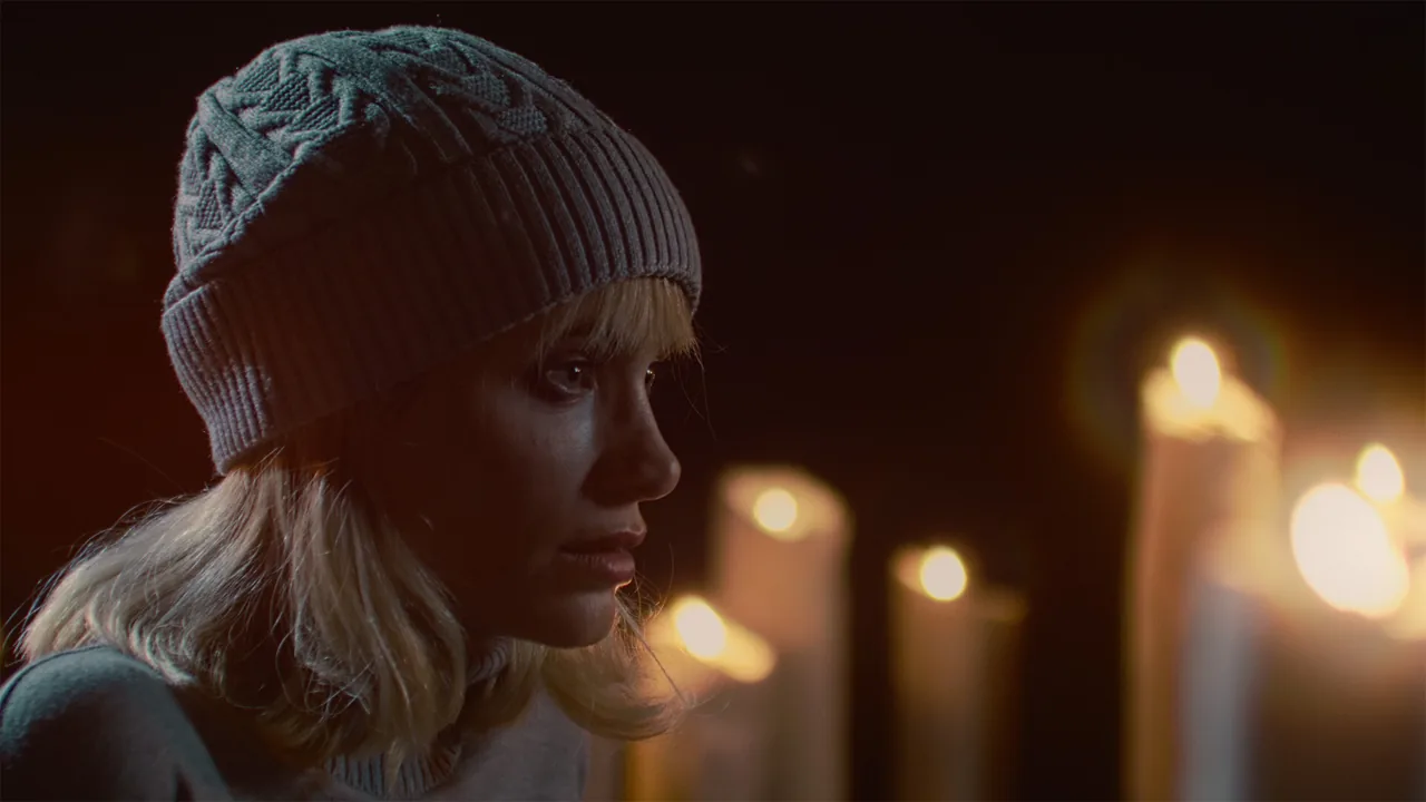 Close-up of a woman in a knitted hat with burning candles behind her